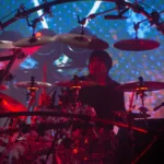 A drummer inside a circular rig at a Chase and Status show under red and blue lighting