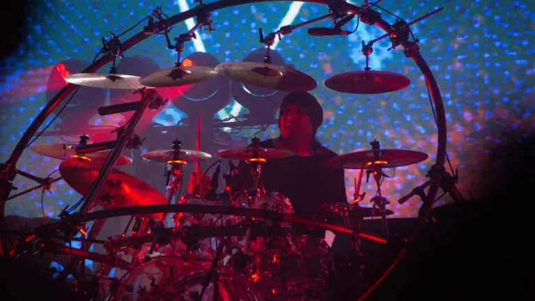 A drummer inside a circular rig at a Chase and Status show under red and blue lighting