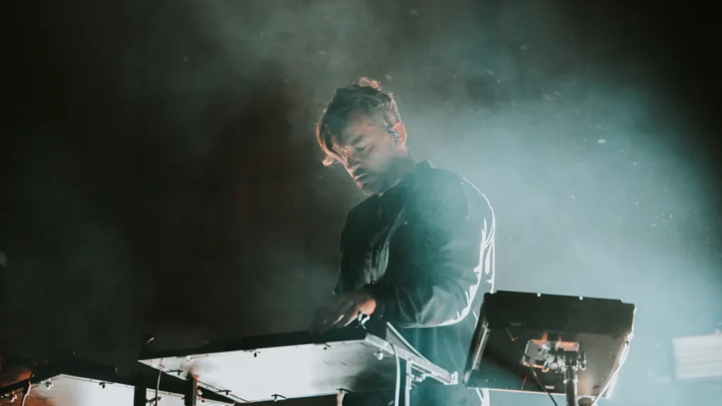 Bonobo performing behind a keyboard in stage haze