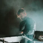 Bonobo performing behind a keyboard in stage haze