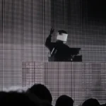 Squarepusher performing in an LED visor mask in front of a large screen