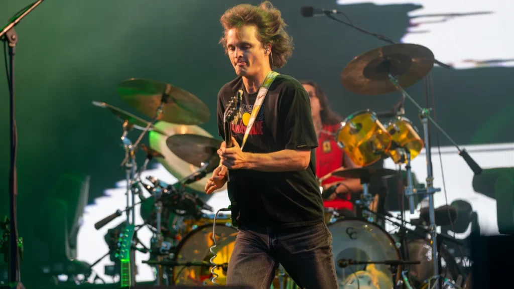 Stu Mackenzie of King Gizzard mid-stride with a guitar under green stage lighting