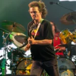 Stu Mackenzie of King Gizzard mid-stride with a guitar under green stage lighting