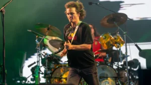 Stu Mackenzie of King Gizzard mid-stride with a guitar under green stage lighting